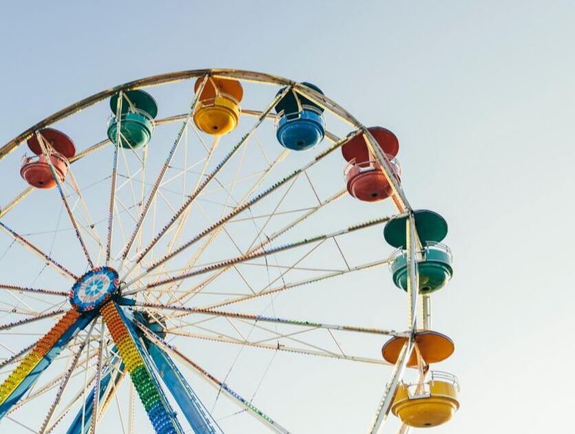 Fotografia de uma parte de uma roda-gigante numa feira popular. São visíveis seis compartimentos, todos com cores garridas, vermelho, verde, amarelo e azul. O fundo é um céu limpo.